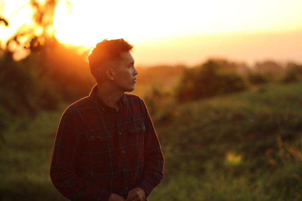 Man in a field with sun setting behind him